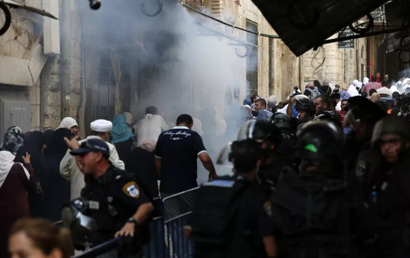 Israeli security forces stand guard as Palestinians walk away from tear gas smoke during clashes between Palestinians and Israeli police at Al-Aqsa mosque compound in Jerusalem's Old City on September 13, 2015, just hours before the start of the Jewish New Year. The disturbances came with tensions running high after Israeli Defence Minister Moshe Yaalon last week outlawed the Murabitat (for females) and Murabitun groups which are made up of east Jerusalem Palestinians and Israeli Arabs and who confront Jewish visitors to the volatile Al-Aqsa mosque complex, considered Islam's third holiest shrine.   AFP PHOTO / AHMAD GHARABLI