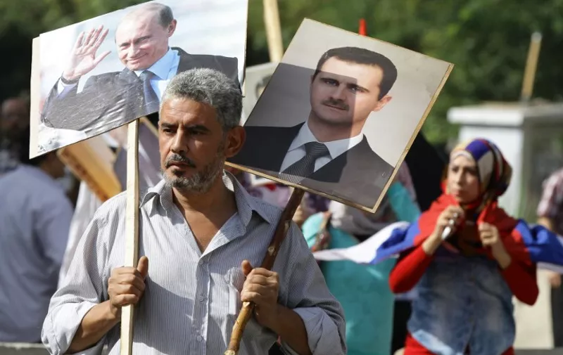 A Syrian man holding up portraits of President Bashar al-Assad and his Russian counterpart Valdimir Putin (L) joins several hundred people who gathered near the Russian embassy in Damascus on October 13, 2015 to express their support for Moscow's air war in Syria, just before two rockets struck the embassy compound sparking panic among the crowd.   AFP PHOTO/LOUAI BESHARA / AFP / LOUAI BESHARA