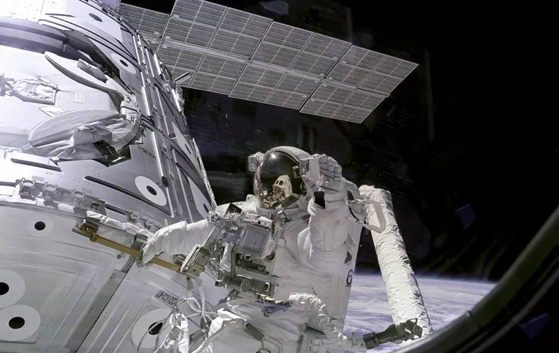 Američki astronaut James Newman, koji je član posade na misiji STS-88 tijekom svoje "svemirske šetnje". Newman se drži za rukohvat ISS-a, a pritom maše kameri koja se nalazi unutar ISS-a.