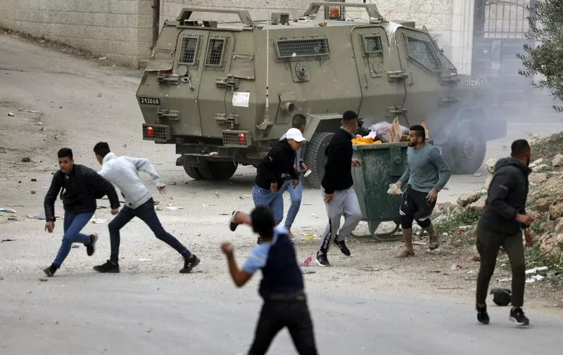 Palestinians throw stones towards Israeli military vehicles during an army raid in the village of Salem, east of Nablus, in the occupied West Bank, on December 14, 2022. (Photo by JAAFAR ASHTIYEH / AFP)