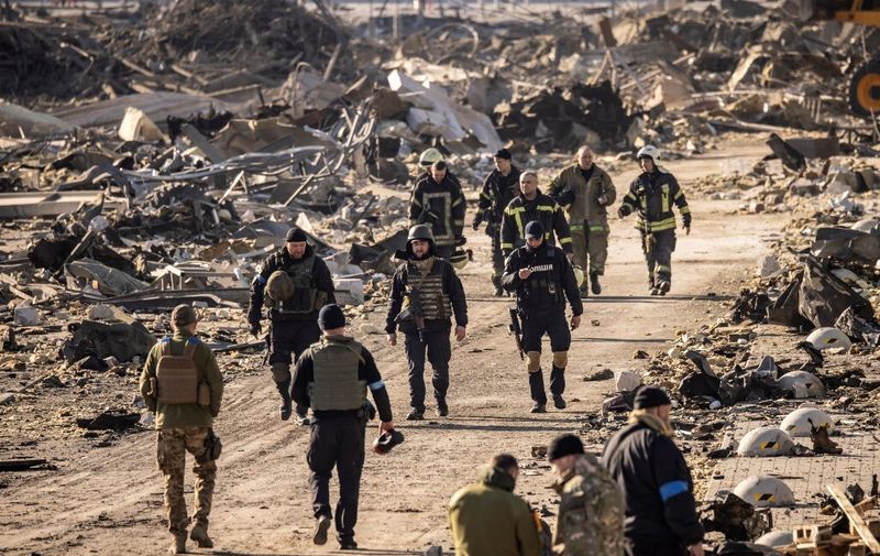 Ukrainian firefighters and servicemen walk amid the rubble of the Retroville shopping mall, a day after it was shelled by Russian forces in a residential district in the northwest of the Ukranian capital Kyiv on March 21, 2022. - At least six people were killed in the bombing. Six bodies were laid out in front of the shopping mall, according to an AFP journalist. The building had been hit by a powerful blast that pulverised vehicles in its car park and left a crater several metres wide. (Photo by FADEL SENNA / AFP)