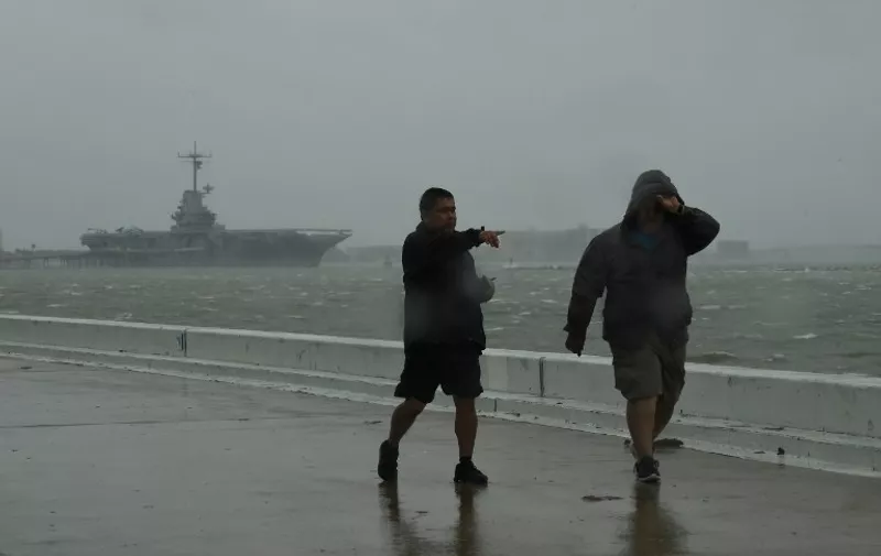 Local residents walk through strong winds beside the Lexington aircraft carrier before the approaching Hurricane Harvey in Corpus Christi, Texas on August 25, 2017.
Hurricane Harvey will soon hit the Texas coast with forecasters saying it is possible expect up to 3 feet of rain and 125 mph winds. / AFP PHOTO / MARK RALSTON