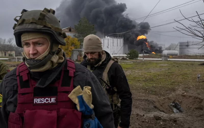 A Ukrainian rescue service member and a soldier inspect the area as black smoke rises after an attack on an oil reserve in Kherson on November 20, 2022, amid the Russian invasion of Ukraine. (Photo by BULENT KILIC / AFP)