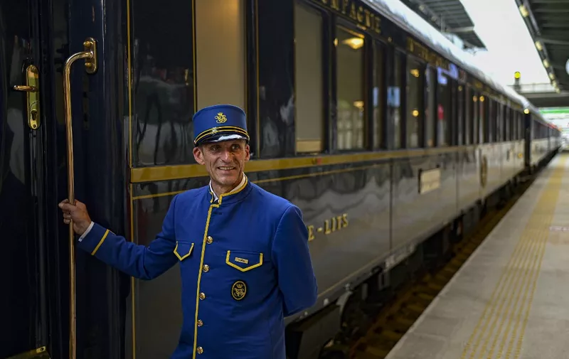 Gabriel, an employee poses with the Venice Simplon-Orient-Express at Istanbul Station, in Istanbul, on August 31, 2022. - The Venice Simplon Orient-Express luxury train arrives in Istanbul, completing its annual voyage along a mythical route that takes it across Europe from Paris. (Photo by Yasin AKGUL / AFP)