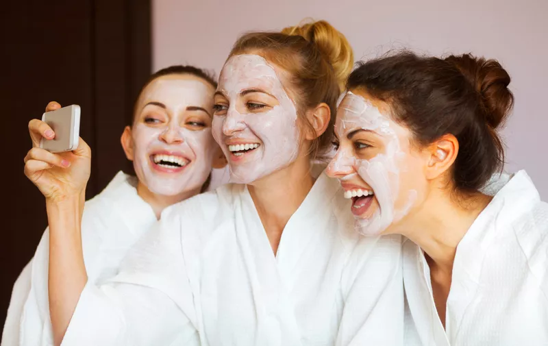 Three young happy women with face masks taking selfie at spa resort. Friendship and wellbeing concept