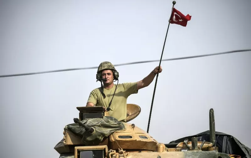 This picture taken around 5 kilometres west from the Turkish Syrian border city of Karkamis in the southern region of Gaziantep, on August 25, 2016 shows a soldier gesturing as Turkish Army tanks drive to the Syrian Turkish border town of Jarabulus.
Turkey's army backed by international coalition air strikes launched an operation involving fighter jets and elite ground troops to drive Islamic State jihadists out of a key Syrian border town. The air and ground operation, the most ambitious launched by Turkey in the Syria conflict, is aimed at clearing jihadists from the town of Jarabulus, which lies directly opposite the Turkish town of Karkamis. / AFP PHOTO / BULENT KILIC