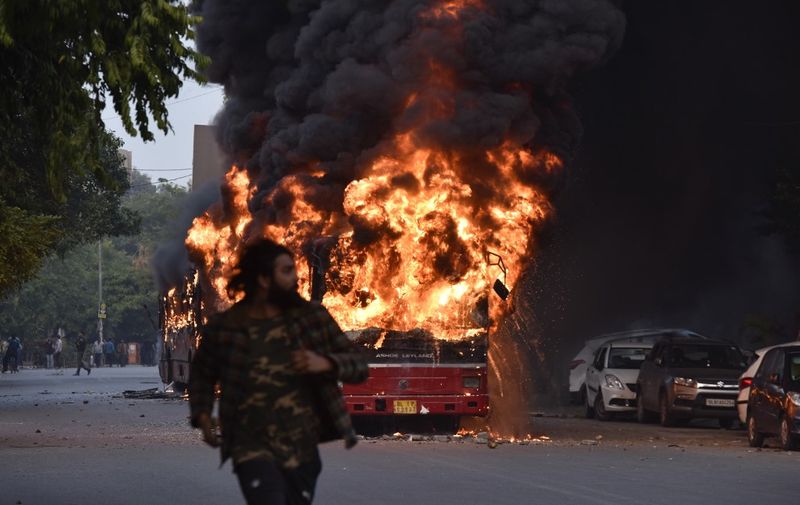 A man walks on a street as a bus is on fire following a demonstration against the Indian government's Citizenship Amendment Bill (CAB) in New Delhi on December 15, 2019. - Angry protesters in northeast India vowed on December 15 to keep demonstrating against a contentious citizenship law as the death toll from bloody clashes opposing the bill rose to six. (Photo by STR / AFP)