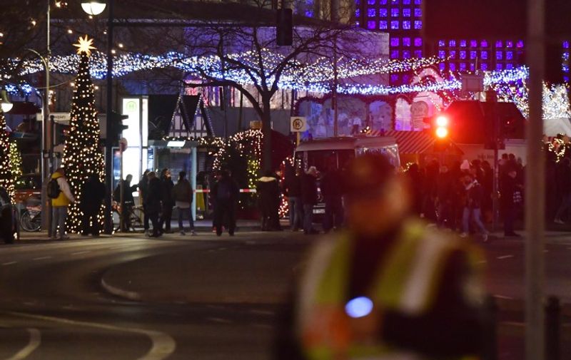 People stand at the scene where a truck speeded into a christmas market in Berlin, on December 19, 2016 killing nine persons and injuring at least 50 people. / AFP PHOTO / John MACDOUGALL