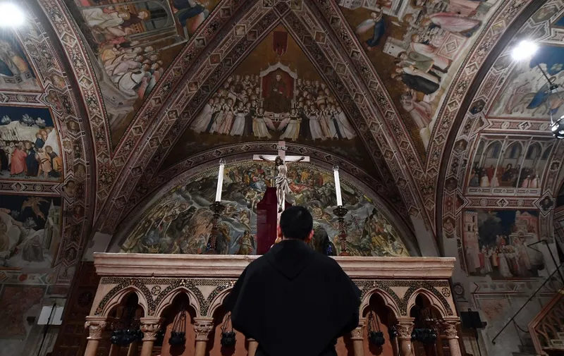 A priest prays by a crucifix within Good Friday Mass at the "Basilica inferior", the lower basilica of Saint Francis of Assisi on April 10, 2020 during the country's lockdown aimed at curbing the spread of the COVID-19 infection, caused by the novel coronavirus. (Photo by Tiziana FABI / AFP)