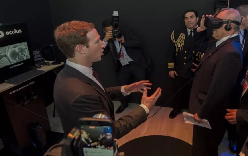 Facebook founder and CEO Mark Zuckerberg looks at Peru's President Pedro Pablo Kuczynski trying a virtual reality headset while visiting the Facebook exhibition booth during the Asia-Pacific Economic Cooperation (APEC) Summit in Lima on November 19, 2016. / AFP PHOTO / AFP / POOL / Pablo PORCIUNCULA