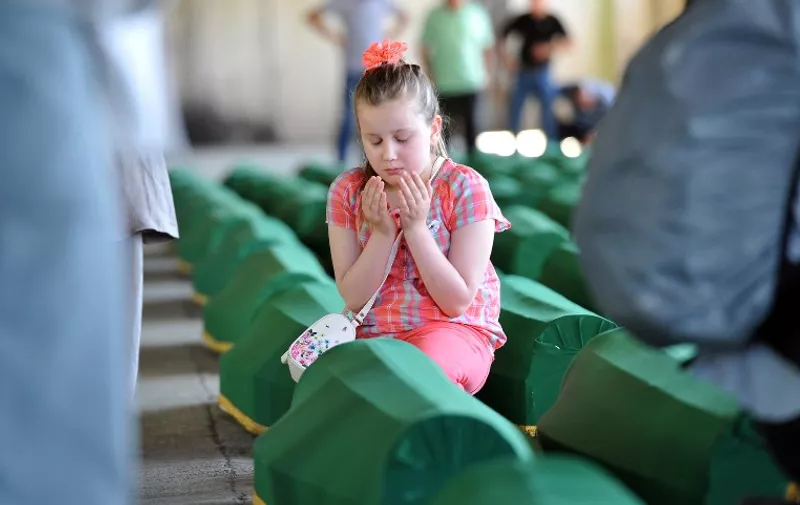 A Bosnian girl prays near the coffin of a relative among 136 others put in a warehouse in Potocari near Srebrenica on July 10, 2015. 136 bodies found in mass grave sites in eastern Bosnia will be reburied at the Potocari memorial cemetery as part of the 20th anniversary of the Srebrenica massacre. Nearly 8,000 men and boys from the enclave were captured and systematically killed by Bosnian Serb forces in the days after the fall of Srebrenica on July 11, 1995. AFP PHOTO / ELVIS BARUKCIC