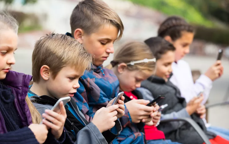 Group of children posing at urban street with mobile devices in spring