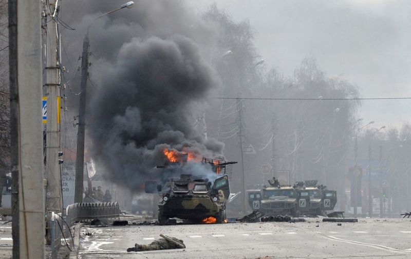 This photograph taken on February 27, 2022 shows a Russian Armoured personnel carrier (APC) burning next to unidentified soldier's body during fight with the Ukrainian armed forces in Kharkiv. - Ukrainian forces secured full control of Kharkiv on February 27, 2022 following street fighting with Russian troops in the country's second biggest city, the local governor said. (Photo by Sergey BOBOK / AFP) / The mention [next to unidentified soldier's body] has been added to the caption and the erroneous mention[s] appearing in the metadata of this photo by Sergey BOBOK has been modified in AFP systems in the following manner: [February 27] instead of [February 26]. Please immediately remove the erroneous mention[s] from all your online services and delete it (them) from your servers. If you have been authorized by AFP to distribute it (them) to third parties, please ensure that the same actions are carried out by them. Failure to promptly comply with these instructions will entail liability on your part for any continued or post notification usage. Therefore we thank you very much for all your attention and prompt action. We are sorry for the inconvenience this notification may cause and remain at your disposal for any further information you may require.