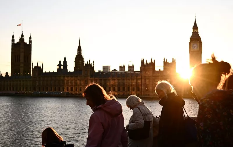 Members of the public stand in line as they queue along the South Bank, with the Palace of Westminster, house of Parliaments and Elizabeth Tower, commonly referred to as Big ben, on the background, to pay their respects to the late Queen Elizabeth II, who is lying-in-state at Westminster Hall, in London, at sunset on September 16, 2022. - Queen Elizabeth II will lie in state at the Palace of Westminster until 0530 GMT on September 19, a few hours before her funeral, with huge queues expected to file past her coffin to pay their respects. (Photo by Marco BERTORELLO / AFP)
