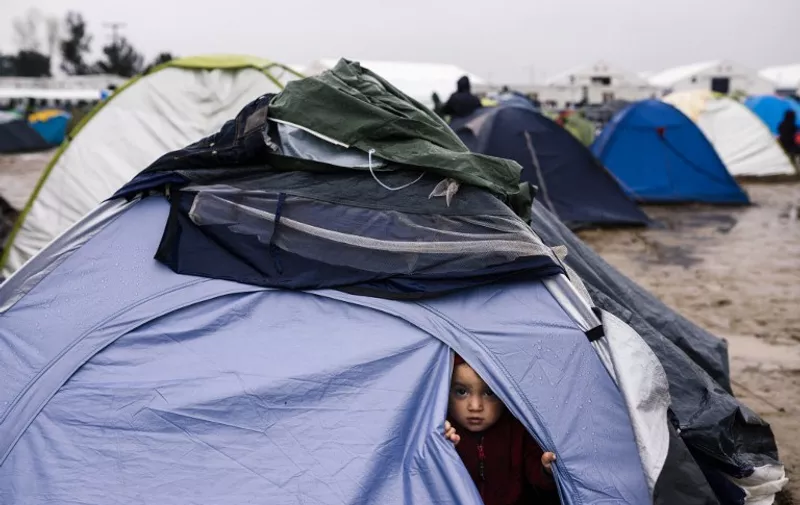 A migrant child looks out from a tent on March 10, 2016, at a makeshift camp of the Greek-Macedonian border, near the Greek village of Idomeni, where thousands of refugees and migrants are stranded by the Balkan border blockade. 
The main migrant trail from Greece to northern Europe was blocked March 9 after western Balkan nations slammed shut their borders, hiking pressure for an EU-Turkey deal and exacerbating a dire situation on the Macedonian border. More than 14,000 mainly Syrian and Iraqi refugees are camping out by the northern Idomeni border crossing with Macedonia -- many of them for weeks -- at a muddy, unhygienic camp operated by beleaguered aid groups.    / AFP / DIMITAR DILKOFF