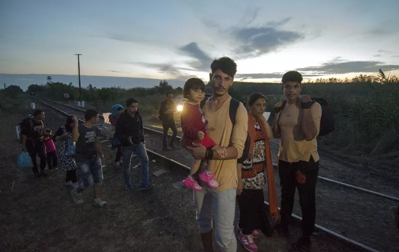 A migrant family walk between the rails near the border village Asotthalom, at the Hungarian-Serbian border on August 24, 2015 as the metal fence was cut by migrants. At least 2,000 more migrants flooded overnight into Serbia in a desperate journey to try and go on to Hungary, the door into the European Union, a UN official said on August 24, 2015. AFP PHOTO / CSABA SEGESVARI