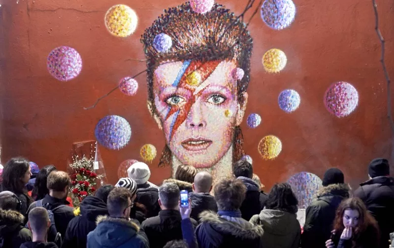 Crowds gather to read and place floral tributes beneath a mural of British singer David Bowie, painted by Australian street artist James Cochran, aka Jimmy C, following the announcement of Bowie's death, in Brixton, south London, on January 11, 2016. British music icon David Bowie died of cancer at the age of 69, drawing an outpouring of tributes for the innovative star famed for groundbreaking hits like "Ziggy Stardust" and his theatrical shape-shifting style. 
AFP PHOTO / NIKLAS HALLE'N

RESTRICTED TO EDITORIAL USE, MANDATORY MENTION OF THE ARTIST UPON PUBLICATION, TO ILLUSTRATE THE EVENT AS SPECIFIED IN THE CAPTION / AFP / NIKLAS HALLE'N