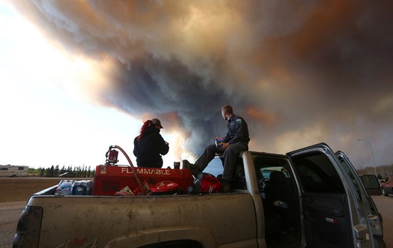 A group trying to rescue animals from Fort McMurray wait at  road block on Highway 63 as smoke rises from a forest fire near Fort McMurray, Alberta on May 6, 2016. 
Canadian police led convoys of cars through the burning ghost town of Fort McMurray Friday in a risky operation to get people to safety far to the south.In the latest chapter of the drama triggered by monster fires in Alberta's oil sands region, the convoys of 50 cars at a time are driving through the city at about 50-60 kilometers per hour (30-40 miles per hour) TV footage showed.
 / AFP PHOTO / Cole Burston/