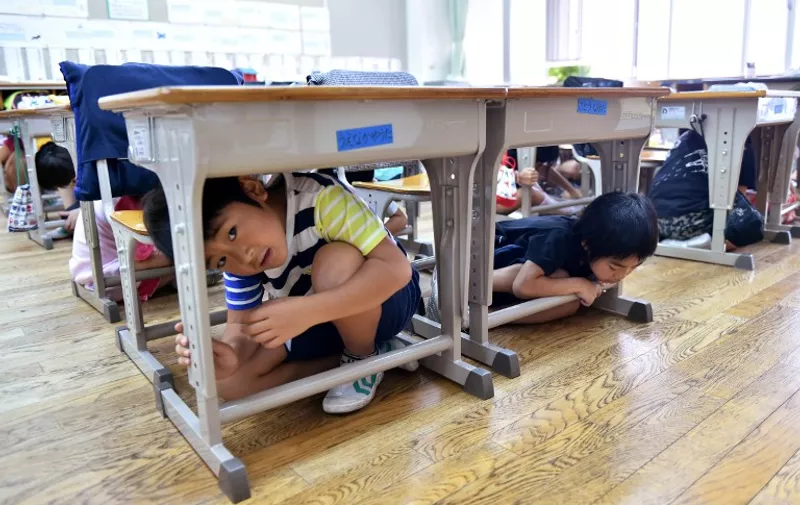 Elementary school children take cover under their desks during an earthquake drill at a school in Tokyo on September 1, 2015. Nationwide anti-disaster drills were held on September 1 on the anniversary of the massive 1923 earthquake which killed more than 100,000 people in the Tokyo metropolitan area.   AFP PHOTO/Yoshikazu TSUNO / AFP / YOSHIKAZU TSUNO