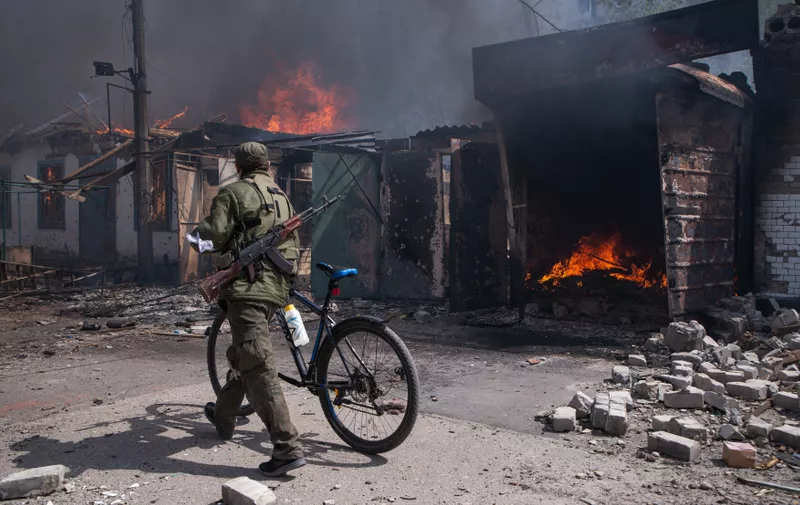 LUGANSK REGION, UKRAINE - MAY 10, 2022: A serviceman of the Lugansk People's Republic militia pushes a bicycle past burning structures in a market in the town of Popasnaya which came under control of the Lugansk People's Republic on 8 May. The Russian Armed Forces are carrying out a special military operation in Ukraine in response to requests from the leaders of the Donetsk People's Republic and Lugansk People's Republic for assistance. Alexander Reka/TASS,Image: 690096484, License: Rights-managed, Restrictions: , Model Release: no, Credit line: Profimedia