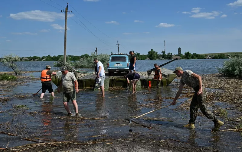 Ukrainian servicemen prepare to unload residents and a car evacuated on a pontoon from the flooded village of Afanasiivka, Mykolaiv region on June 9, 2023, after water level in the Ingulets river increased following damages sustained at Kakhovka hydroelectric power plant dam. Ukraine and Russia accused each other of shelling in the flood hit Kherson region even as rescuers raced to save people stranded after the destruction of a Russian-held dam flooded towns and villages along the banks of the Dnipro river, including neighbourhoods of the regional capital Kherson, forcing thousands of people to evacuate their homes. (Photo by Genya SAVILOV / AFP)
