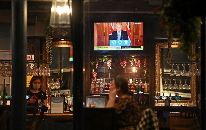 A television shows Britain's Prime Minister Boris Johnson speaking from 10 Downing Street in London, as customers sit at the bar inside the William Gladstone pub in Liverpool, north west England on October 12, 2020, following the announcement of new local lockdown measures to be imposed to help stem a second wave of the novel coronavirus COVID-19. - British Prime Minister Boris Johnson presented a new three-tiered alert system for coronavirus cases in England on Monday, with Liverpool in the northwest expected to be the only city placed in the top category. Like governments throughout Europe, Johnson's conservative cabinet is seeking to balance bringing down the rate of new infections against concern about the economy and frustration among voters. (Photo by Paul ELLIS / AFP)