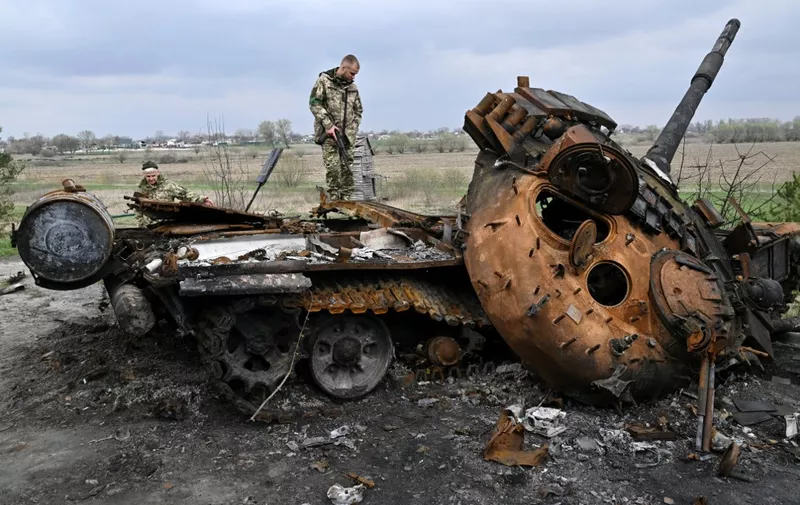 Ukrainian servicemen look at a destroyed Russian tank on a road in the village of Rusaniv, in the Kyiv region on April 16, 2022. - Many of the nearly five million people who have fled Ukraine will not have homes to return to, the United Nations said on April 16, 2022, as another 40,000 fled the country in 24 hours. (Photo by Genya SAVILOV / AFP)