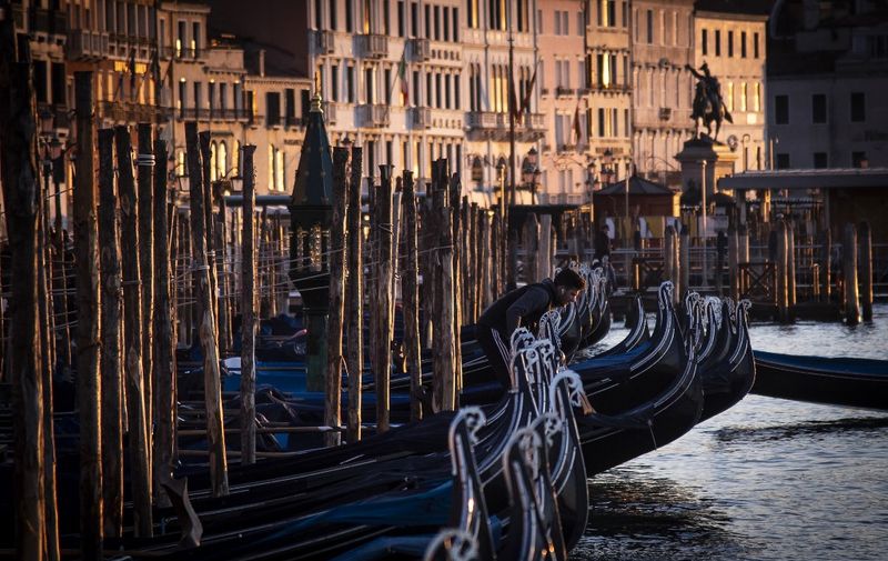 This picture taken on February 13, 2022 shows a man on gondolas moored in the Venice lagoon at the sunrise. (Photo by Tiziana FABI / AFP)