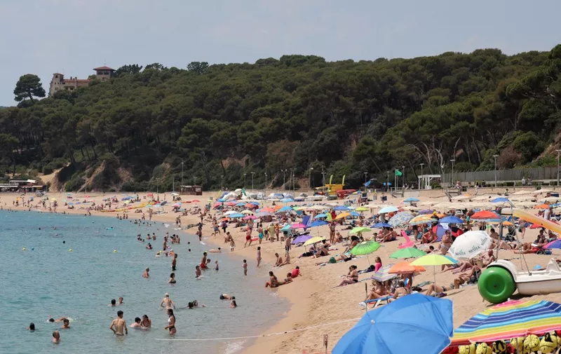 Tourists sunbath and play in water at Fenals beach in Lloret de Mar on June 27, 2023. With Spain at the forefront of the climate crisis in Europe, its key tourism sector is facing growing pressure to reduce its environmental impact and become more sustainable. (Photo by LLUIS GENE / AFP)
