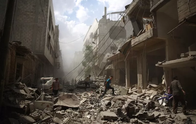 Syrians walk amid the rubble of destroyed buildings following reported air strikes by regime forces in the rebel-held area of Douma, east of the capital Damascus, on August 30, 2015. More than 240,000 people have been killed since Syria's conflict began in March 2011, and half of the country's population has been displaced by the war. AFP PHOTO / ABD DOUMANY