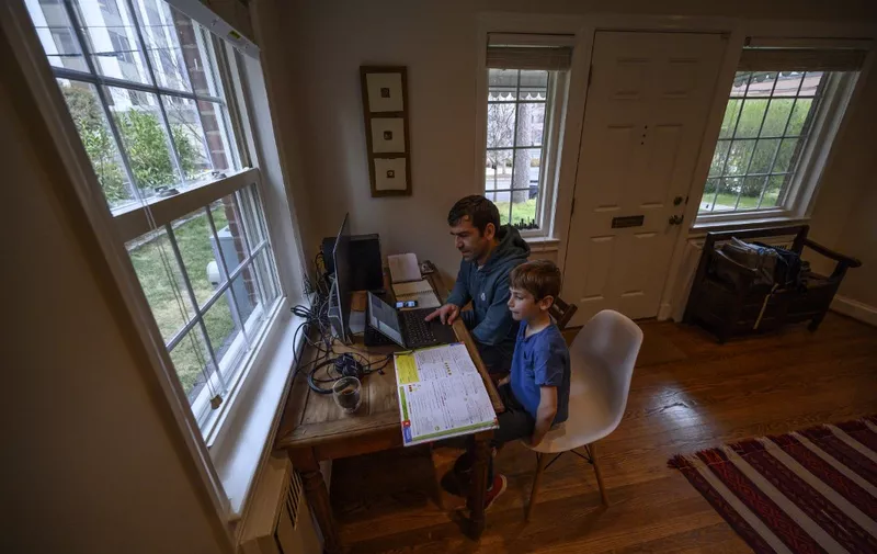 Joachim, 8, whose school was closed following the Coronavirus outbreak, does school exercises at home with his dad Pierre-Yves in Washington on March 20, 2020. - As millions of families hunker down amid the coronavirus crisis, the sudden reality of schooling from home risks widening the education gap between those with the means and support to keep up with lessons, and those who risk falling behind. (Photo by Eric BARADAT / AFP)