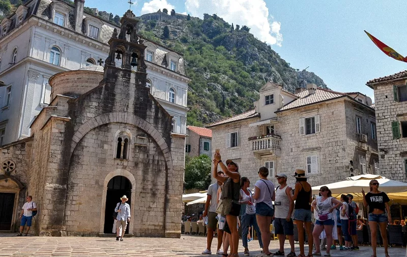 Tourists stand in front of a church as they visit the medieval city of Kotor on August 21, 2018. - Montenegro's medieval walled city of Kotor, an Adriatic seaport cradled in a spectacular fjord-like bay, has survived centuries of weather and warfare. Now it is facing a different kind of assault, that of gargantuan cruise ships disgorging throngs of tourists threatening a place that was only a few years ago commonly described as a "hidden gem". (Photo by Savo PRELEVIC / AFP)