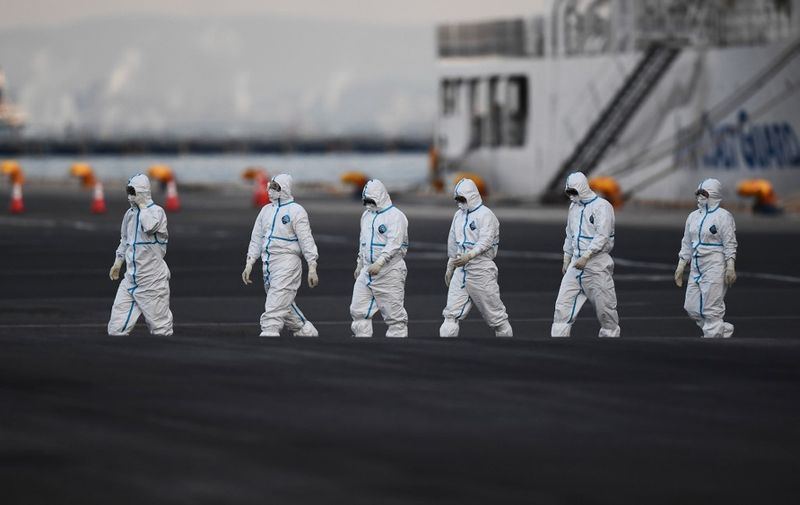 People wearing protective suits walk from the Diamond Princess cruise ship, with around 3,600 people quarantined onboard due to fears of the new coronavirus, at the Daikoku Pier Cruise Terminal in Yokohama port on February 10, 2020. - Around 60 more people on board the quarantined Diamond Princess cruise ship moored off Japan have been diagnosed with novel coronavirus, the country's national broadcaster said on February 10, raising the number of infected passengers and crew to around 130. (Photo by CHARLY TRIBALLEAU / AFP)