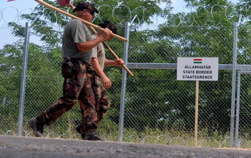 A picture is taken on July 18, 2015 shows soldiers of the Hungarian Army's technical unit passing by a new 'State Border' sign in front of the first completed elements of the 150 meter-long metal fence at the Hungarian-Serbian border nearby Morahalom village. Defense Minister Csaba Hende said that 900 people would work simultaneously to install the fence which is planned to be 4 meters (13 feet) high along the 175-kilometer (109-mile) border between Hungary and Serbia. Over the last two years, Hungary has been one of the main routes for people hoping to cross into Austria and Germany, most coming from Afghanistan, Iraq, Syria and Kosovo. Hungary's defense minister says that a fence on the border with Serbia to stem the flow of migrants and refugees will be built by Nov. 30.  AFP PHOTO / CSABA SEGESVARI
