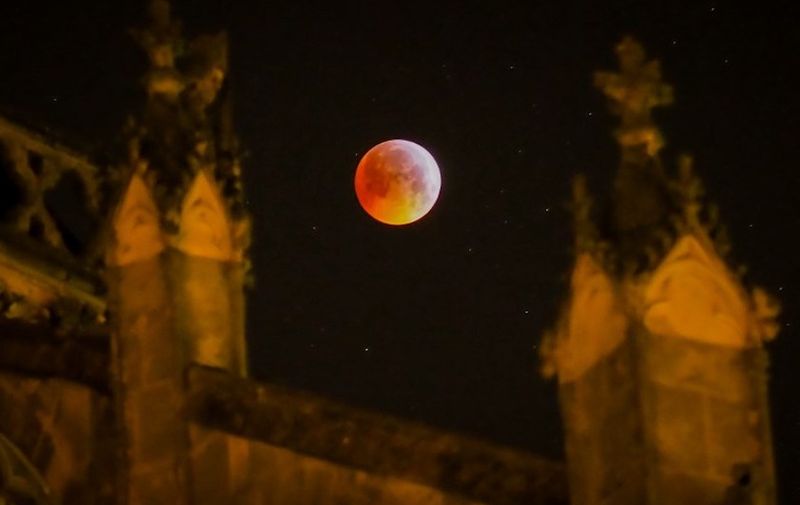 A picture taken on January 21, 2019 shows the so-called Super Blood Wolf Moon behind the Tours's cathedral on January 21, 2019, central France. (Photo by GUILLAUME SOUVANT / AFP)