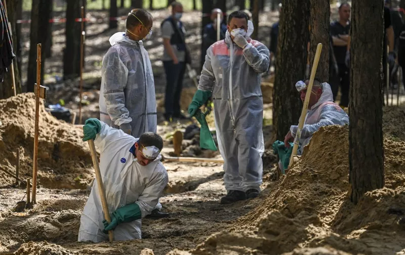 Forensic technicians dig at the site of a mass grave in a forest on the outskirts of Izyum, eastern Ukraine on September 18, 2022. - Ukrainian authorities discovered around 450 graves outside the formerly Russian-occupied city of Izyum with some of the exhumed bodies showing signs of torture. (Photo by Juan BARRETO / AFP)