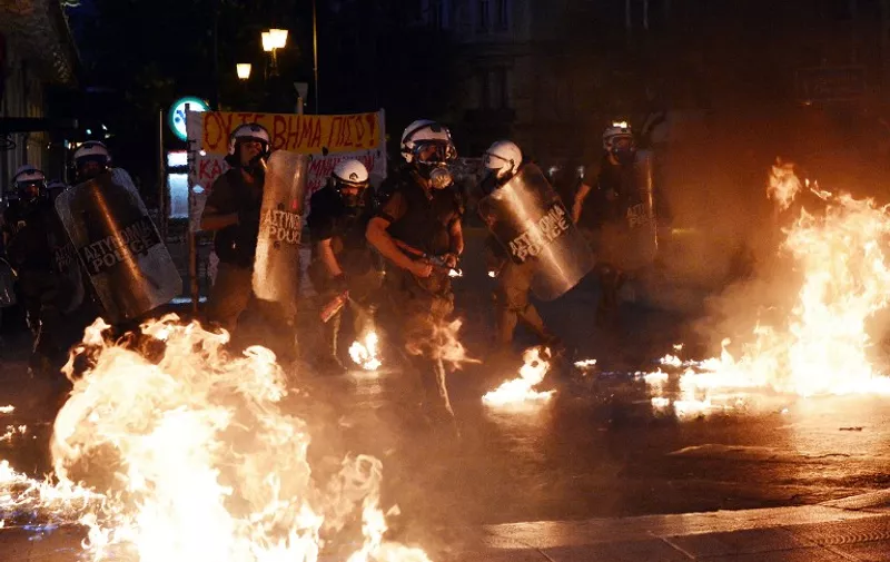 Riot police stand amid petrol bombs threw by protesters during an anti-austerity protest on July 15, 2015. Anti-austerity protesters hurled petrol bombs at police in front of Greece's parliament on Wednesday as lawmakers began debating deeply unpopular reforms needed to unlock a new eurozone bailout.Riot police responded with tear gas against dozens of hooded protesters who set ablaze parts of Syntagma square in central Athens .AFP PHOTO/ LOUISA GOULIAMAKI