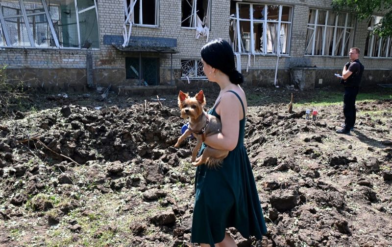 A woman holding a dog stands by a huge crater made from the hit of a rocket close to the destroyed school building in Kharkiv, on July 4, 2022, amid Russian invasion of Ukraine. (Photo by Sergey BOBOK / AFP)
