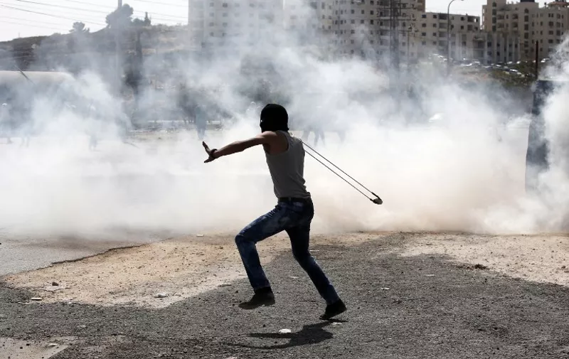 A Palestinian protester uses a slingshot to throw stones towards Israeli security forces during clashes near the Jewish West Bank settlement Beit El, north of Ramallah on October 5, 2015 as violence spiked in east Jerusalem and the occupied West Bank. There have been fears that the sporadic violence could spin out of control, with some warning of the risk of a third Palestinian intifada, or uprising.   AFP PHOTO / ABBAS MOMANI