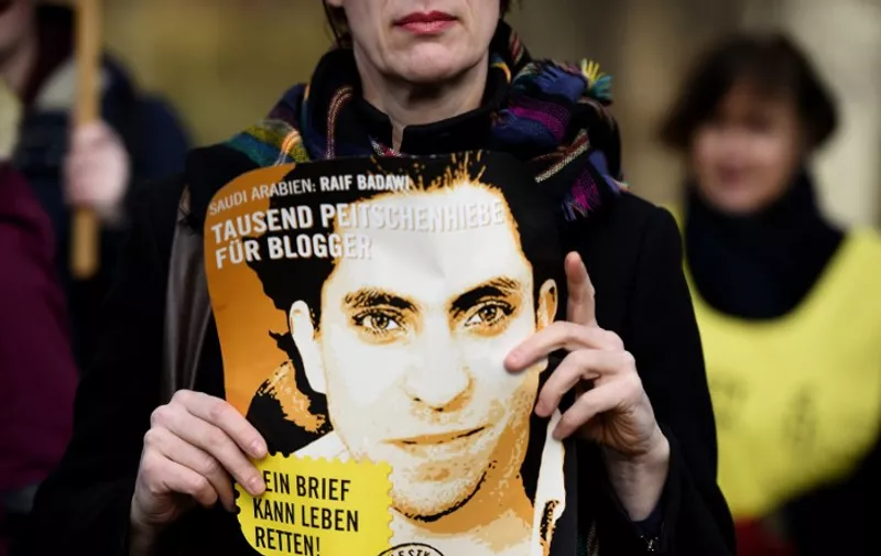 (FILES) - A file picture taken on  January 29, 2015 shows an Amnesty International activist holding a picture of Saudi blogger Raif Badawi during a protest against his flogging punishment  in front of Saudi Arabia's embassy in Berlin. The jailed Saudi blogger who was named winner of the Sakharov prize on October 29, 2015 , is known as a fighter for free speech and  sentenced to 1,000 lashes in his country  for insulting Islam. AFP PHOTO / TOBIAS SCHWARZ