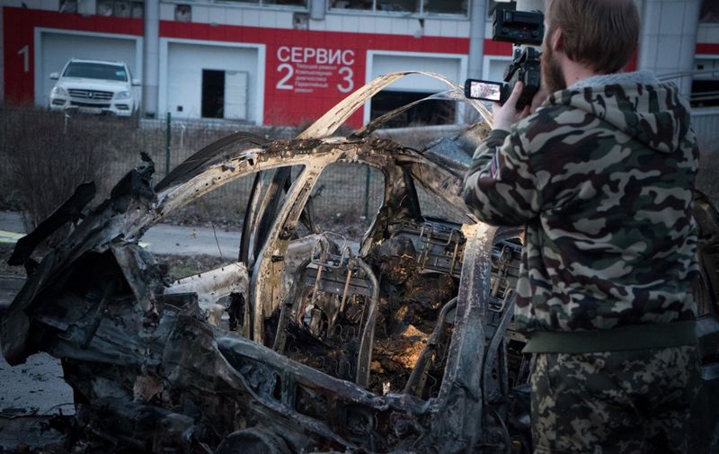 A man films a destroyed car with a burnt body inside it after shelling in Donetsk, eastern Ukrane, on February 4, 2015. At least 12 people were killed in fighting between soldiers and pro-Russian separatists in east Ukraine, including four civilians who died when a hospital was hit in rebel stronghold Donetsk on Februry 4. AFP PHOTO / ANDREY BORODULIN (Photo by ANDREY BORODULIN / AFP)