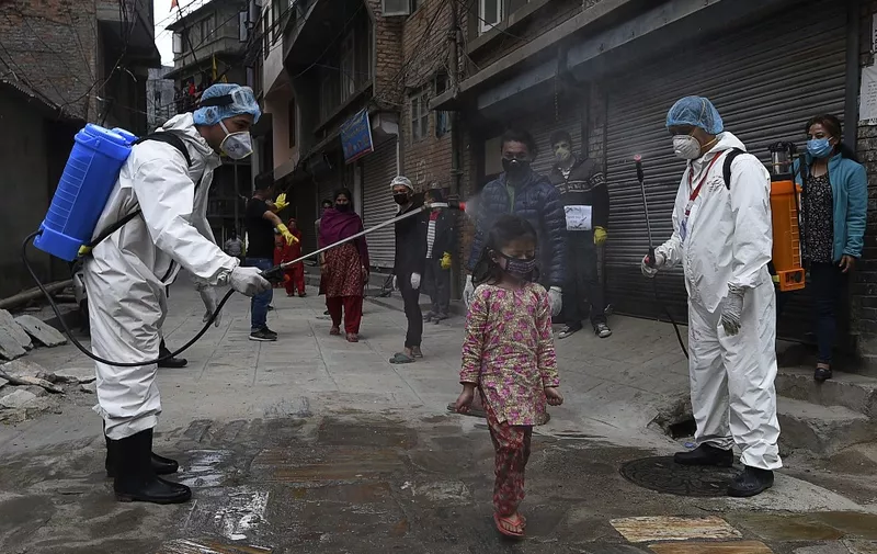 Health workers wearing protective suits spray disinfectant on a young girl during a government-imposed nationwide lockdown as a preventive measure against the COVID-19 coronavirus, on a deserted road in Kathmandu on May 3, 2020. (Photo by PRAKASH MATHEMA / AFP)