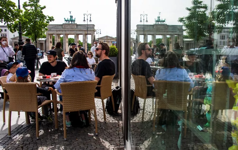 People are reflected in a window as they sit at a cafe terrace near the Brandenburg Gate in Berlin on May 24, 2021, as restaurants and cafes were allowed to resume business outdoors, amid the coronavirus (Covid-19) pandemic. (Photo by John MACDOUGALL / AFP)
