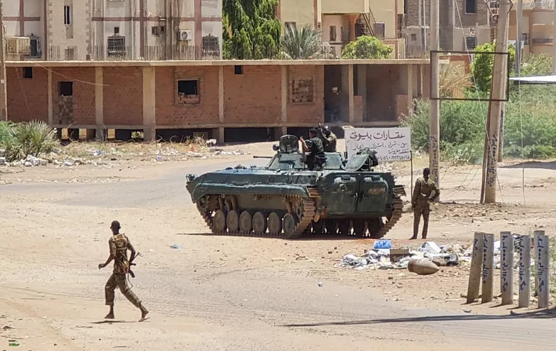 Sudanese Army sodliers walk near armoured vehicles stationed on a street in southern Khartoum, on May 6, 2023, amid ongoing fighting against the paramilitary Rapid Support Forces. - Air strikes battered Sudan's capital on May 6, as fighting entered a fourth week only hours before the warring parties are to meet in Saudi Arabia for their first direct talks. (Photo by AFP)
