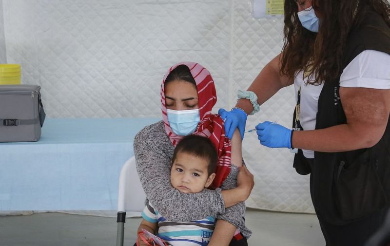 A woman holding her child receives a dose of a Covid-19 vaccine in the refugee camp of Mavrovouni in the Greek island of Lesbos on June 3, 2021. (Photo by Manolis Lagoutaris / AFP)