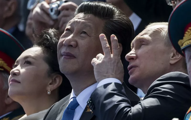 Russian President Vladimir Putin (R) speaks with Chinese President Xi Jinping (C) as they watch the Victory Day military parade at Moscow's Red Square on May 9, 2015. Russian President Vladimir Putin presides over a huge Victory Day parade celebrating the 70th anniversary of the Soviet win over Nazi Germany, amid a Western boycott of the festivities over the Ukraine crisis. AFP PHOTO / POOL / ALEXANDER ZEMLIANICHENKO (Photo by ALEXANDER ZEMLIANICHENKO / POOL / AFP)