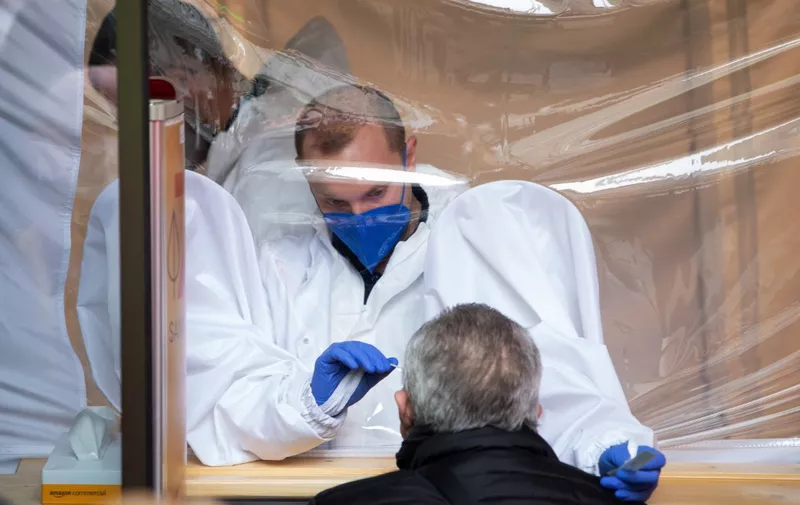 A medical worker from a behind a safety screen takes a quick antigen test of a man in a pharmacy in Vienna on February 8, 2021. - Austria has ended the hard lockdown today and allowed services with the mandatory use of FFP2 protective masks and a negative coronavirus rapid antigen test. (Photo by ALEX HALADA / AFP)