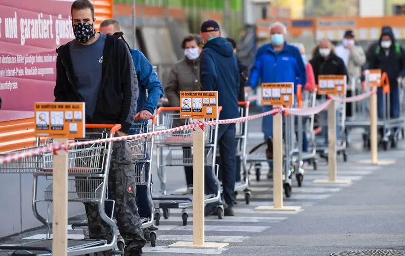 Customers wearing face masks and pushing shopping carts line up in front of a DIY store in Innsbruck, Austria, after it re-opened on April 14, 2020, following a "shutdown" in a measure to limit the spread of the new coronavirus. (Photo by Erich SPIESS / various sources / AFP) / Austria OUT