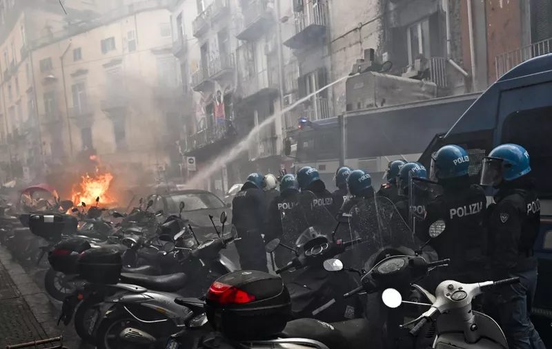This photo obtained from Italian news agency Ansa shows a anti-riot policemen move beside a truck extinguishing the blaze of a police car after it was set on frie during clashes between Eintracht Frankfurt fans and police on March 15, 2023 in downtown Naples prior to the UEFA Champions League round of 16, second leg football match between SSC Napoli and Eintracht Frankfurt to be played at the Diego-Maradona stadium in Naples. Eintracht Frankfurt fans clashed with police on March 15 after arriving in Naples despite not having tickets for their team's Champions League decider with Napoli. (Photo by Ciro FUSCO / ANSA / AFP) / Italy OUT