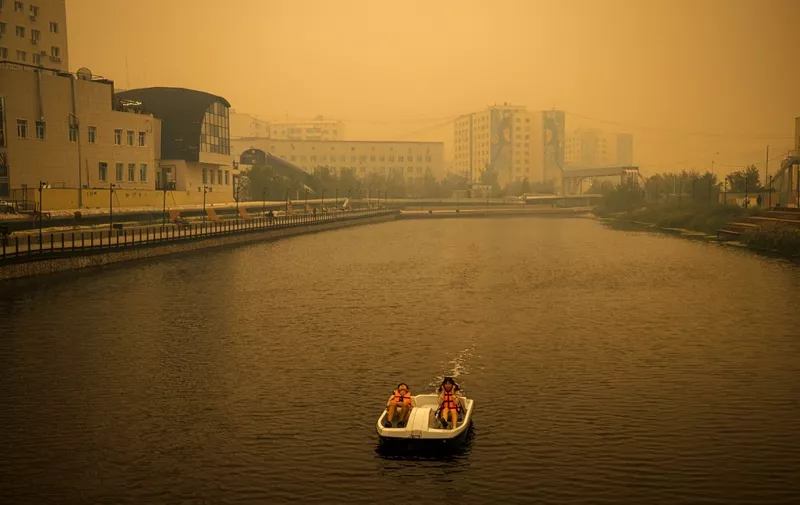 A couple rides a pedal boat as smoke from nearby forest fires hangs over the city of Yakutsk, in the republic of Sakha, Siberia, on July 27, 2021. - Russia is plagued by widespread forest fires, with the Sakha-Yakutia region in Siberia being the worst affected. According to many scientists, Russia -- especially its Siberian and Arctic regions -- is among the countries most exposed to climate change. The country has set numerous records in recent years and in June 2020 registered 38 degrees Celsius (100.4 degrees Fahrenheit) in the town of Verkhoyansk -- the highest temperature recorded above the Arctic circle since measurements began. (Photo by Dimitar DILKOFF / AFP)